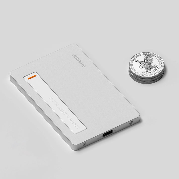 Ein elegantes, silbernes, kartenförmiges Gerät neben einem Stapel Münzen, mit einem USB-C-Anschluss und einer orangefarbenen Anzeige.